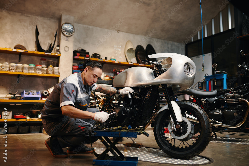 Repairman choosing tool when fixing motorcycle in his repairshop - obrazy, fototapety, plakaty 