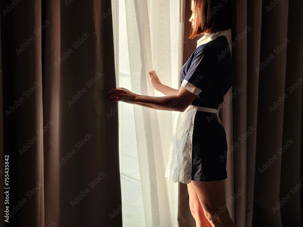 Closeup of a maid opening the curtains on a window in a hotel room.
