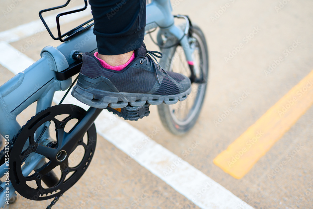 Obraz premium Closeup foot of a woman on the pedal of a folding bicycle, with traffic lines on the asphalt road