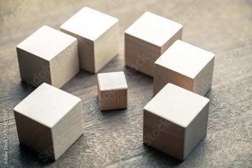 A small wooden cube under siege by many big wooden cubes, concept of a small business encircled by many big ones, high competition, or niche market photo