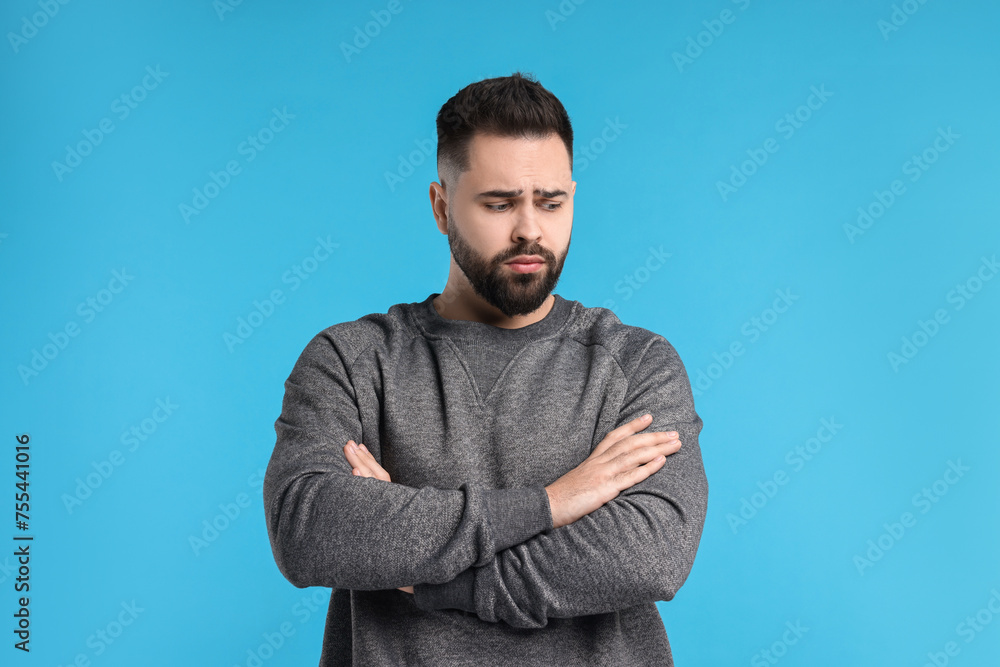 Portrait of sad man with crossed arms on light blue background Portrait of sad man with crossed arms on light blue background