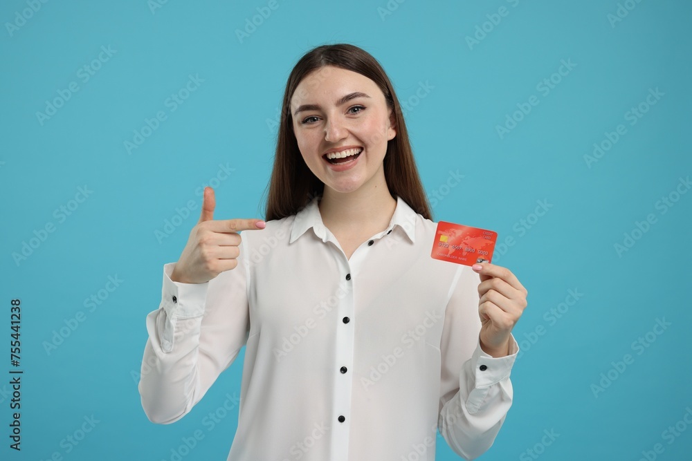 Happy woman pointing at credit card on light blue background Happy woman pointing at credit card on light blue background