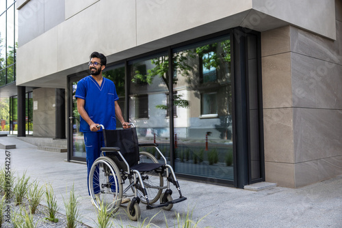 Positive male nurse in blue doctors overall carrying a wheelchair