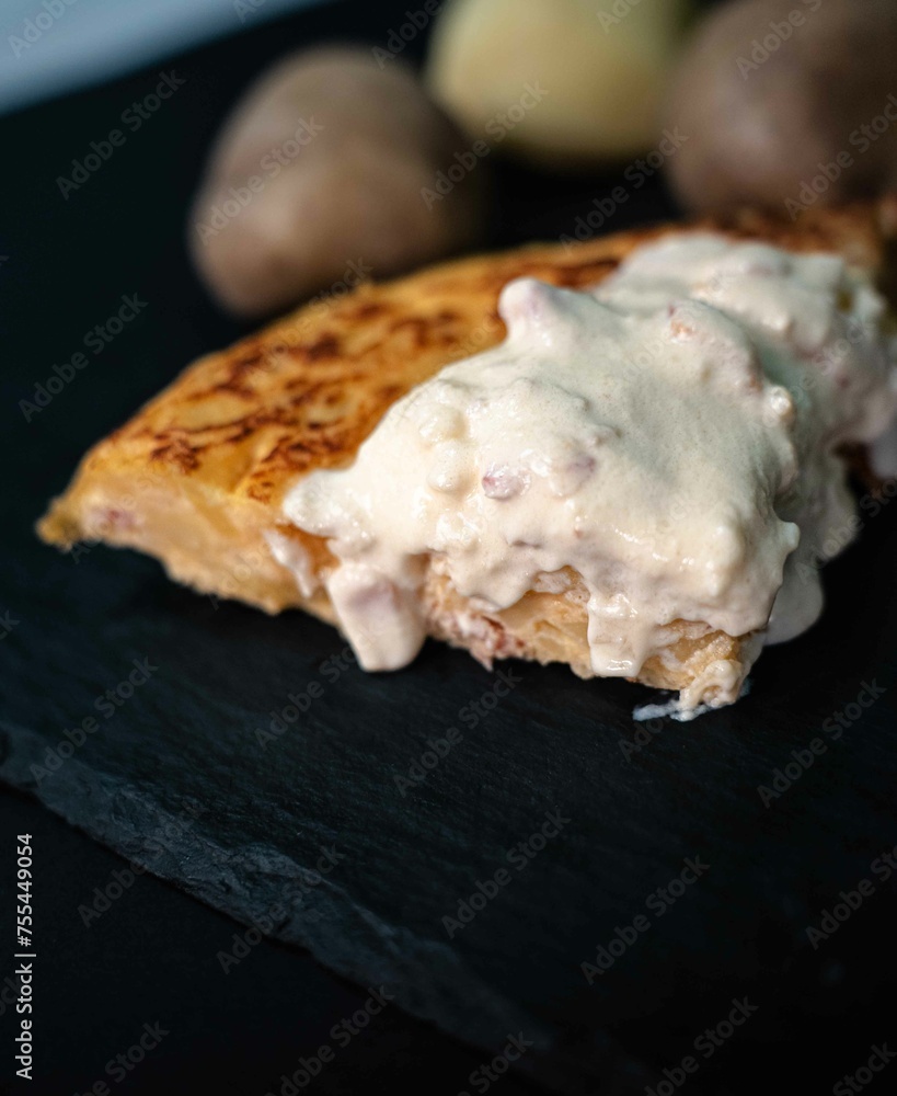 Spanish potato omelette with carbonara sauce, on a white plate, surrounded by the ingredients necessary to prepare it, potatoes, egg, onion and bacon Spanish potato omelette with carbonara sauce, on a white plate, surrounded by the ingredients necessary to prepare it, potatoes, egg, onion and bacon