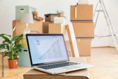 Rising line graph on laptop screen in front of cardboard boxes in an empty room in a new home photo