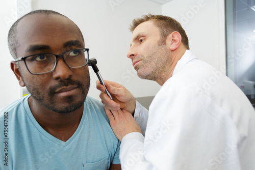 male doctor checking patients ear using otoscope photo