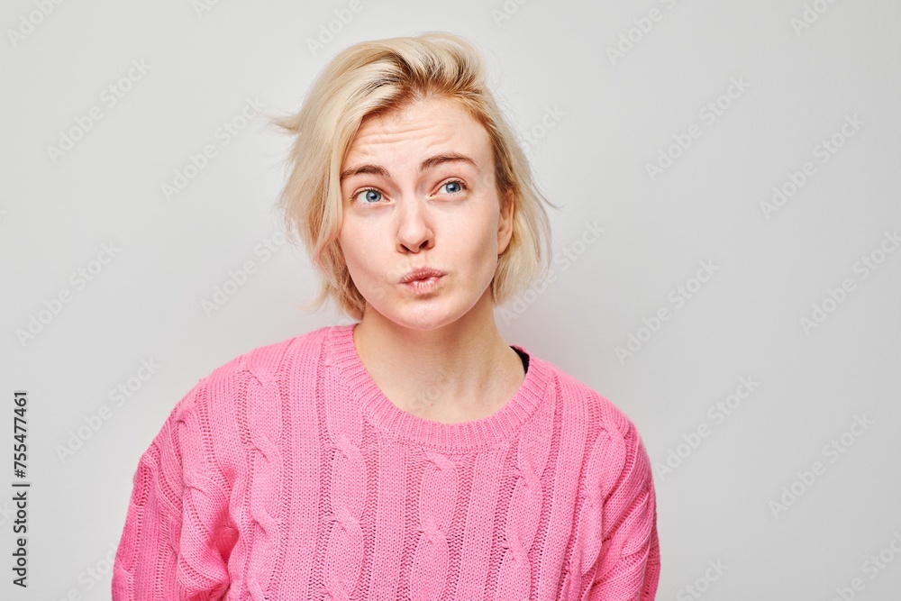 Confused young woman in pink sweater with tousled hair against a grey background. Confused young woman in pink sweater with tousled hair against a grey background.