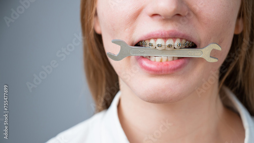 Close-up portrait of a woman with braces holding a wrench in her teeth. 