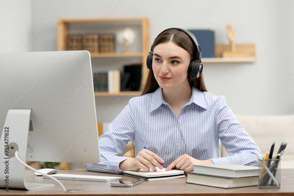 E-learning. Young woman taking notes during online lesson at table indoors E-learning. Young woman taking notes during online lesson at table indoors