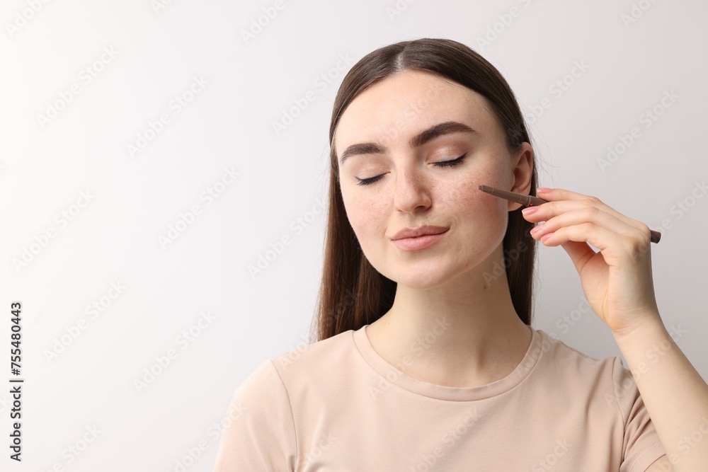 Beautiful woman drawing freckles with pen on light background. Space for text Beautiful woman drawing freckles with pen on light background. Space for text