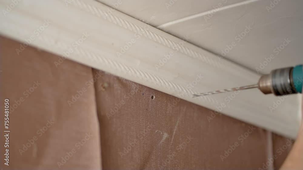 Man drills wall with hammer drill in his home, close up. Economical renovation in old apartment. Male drills wall to hang cornice Man drills wall with hammer drill in his home, close up. Economical renovation in old apartment. Male drills wall to hang cornice