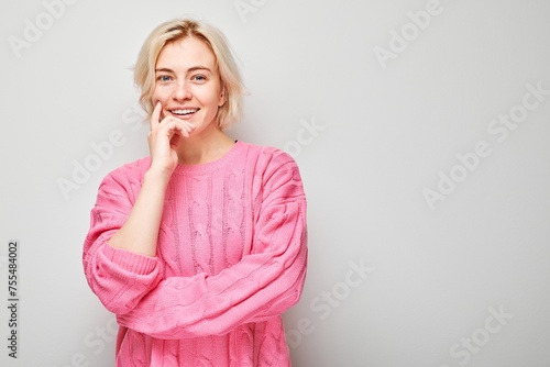 Portrait of smiling woman in pink sweater with a hand on her chin against a light grey background.