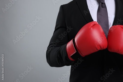 Businessman in suit wearing boxing gloves on grey background, closeup. Space for text © New Africa