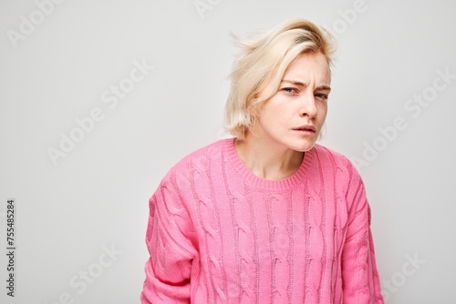 Woman in pink sweater looking away with a thoughtful expression, isolated on a light background. © amixstudio