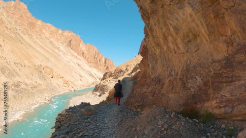 4K shot of an Indian male hiker walking on the trail besides the mountain and blue Tsarap Chu river on the way towards Phugtal Gompa in Zanskar Valley, Ladakh, India. Man trekking in the Himalayas. photo