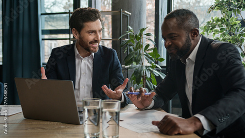 Caucasian businessman insurance agent consult African American male client advise financial offers showing presentation on laptop. Two diverse businessmen men at office discuss project with computer