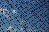 Looking up at a chain link fence with blue sky and clouds. wire fence. Chain link fence see sky. Opening in metallic fence. blue sky. Challenge. breakthrough concept