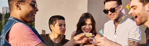 jolly multicultural friends drinking tequila with fresh lime and salt at rooftop party, banner photo