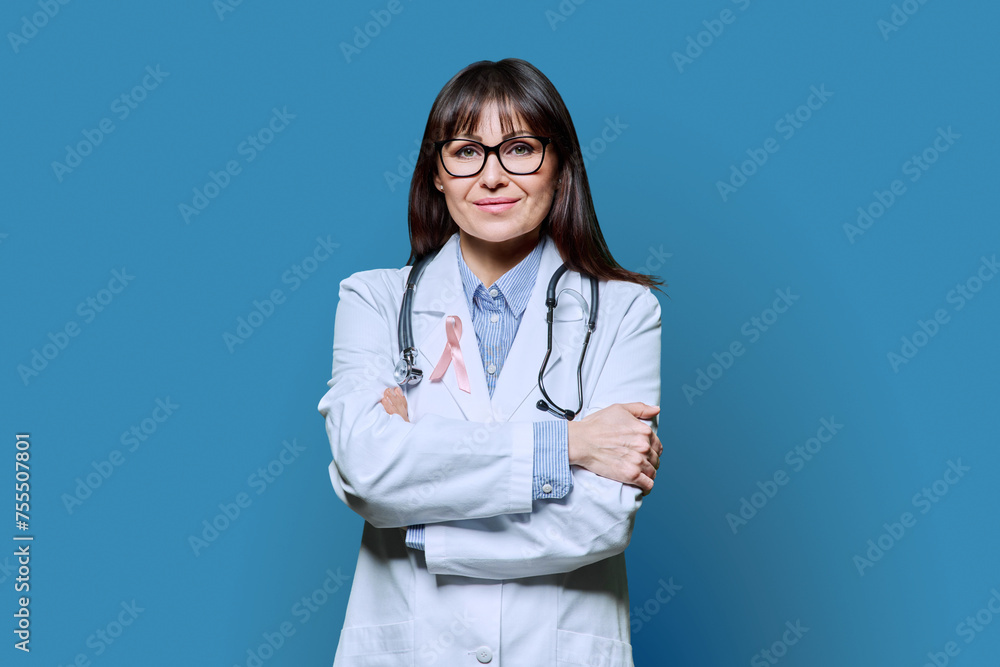 Portrait of female doctor in white coat with pink ribbon on blue background Portrait of female doctor in white coat with pink ribbon on blue background