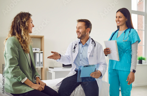 Smiling woman patient talking with man doctor and female friendly nurse holding report file with appointment sitting on the couch in clinic on medical examination. Health care concept.