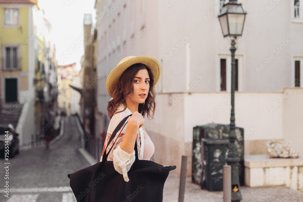 Fototapeta premium Young woman in a pink dress and a straw hat walking around Lisbon streets in summer