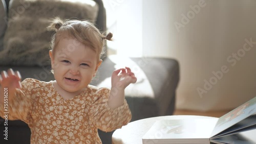 Little baby girl is waving and smiling. The baby is dressed in a beautiful dress and has a cute hairstyle