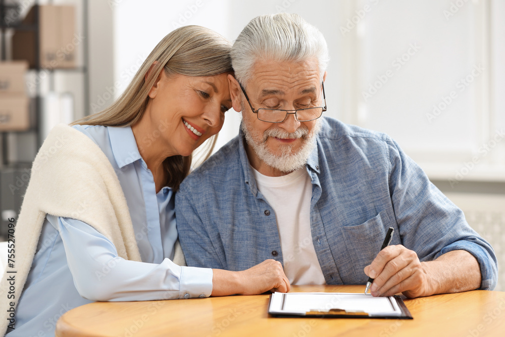 Happy senior couple signing Last Will and Testament indoors Happy senior couple signing Last Will and Testament indoors