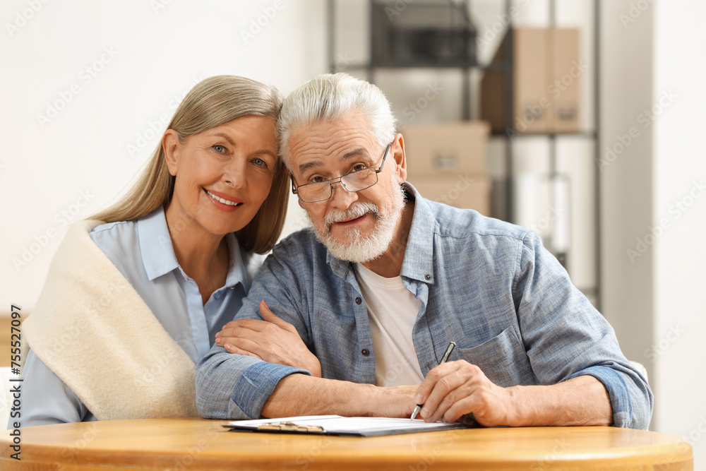 Smiling senior couple signing Last Will and Testament indoors