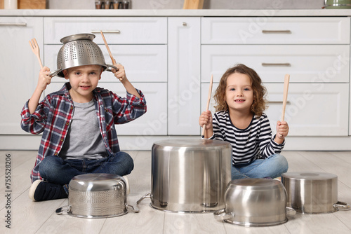 Tableau sur toile Little children pretending to play drums on pots in kitchen