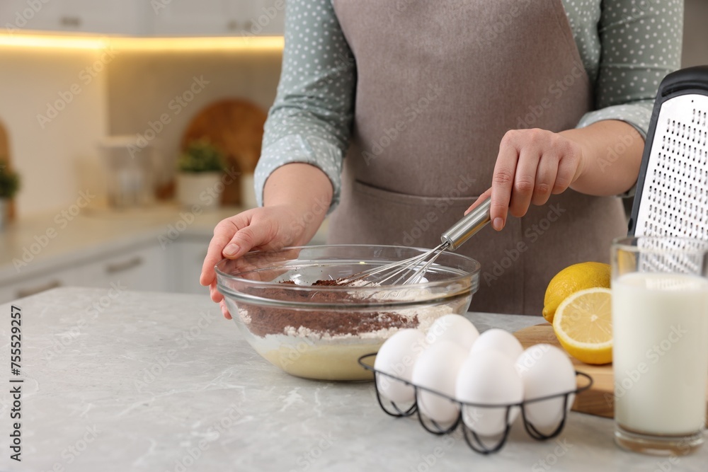 Woman making chocolate dough with whisk in bowl at gray marble table, closeup