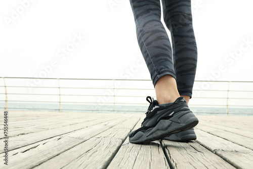 Female legs in leggings and sneakers on wooden floor outdoors, close up photo