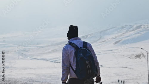 indian man with backpack dipping bike helmet in the puddle near snow mountains at gulmarg, jammu and kashmir, india. 4k photo