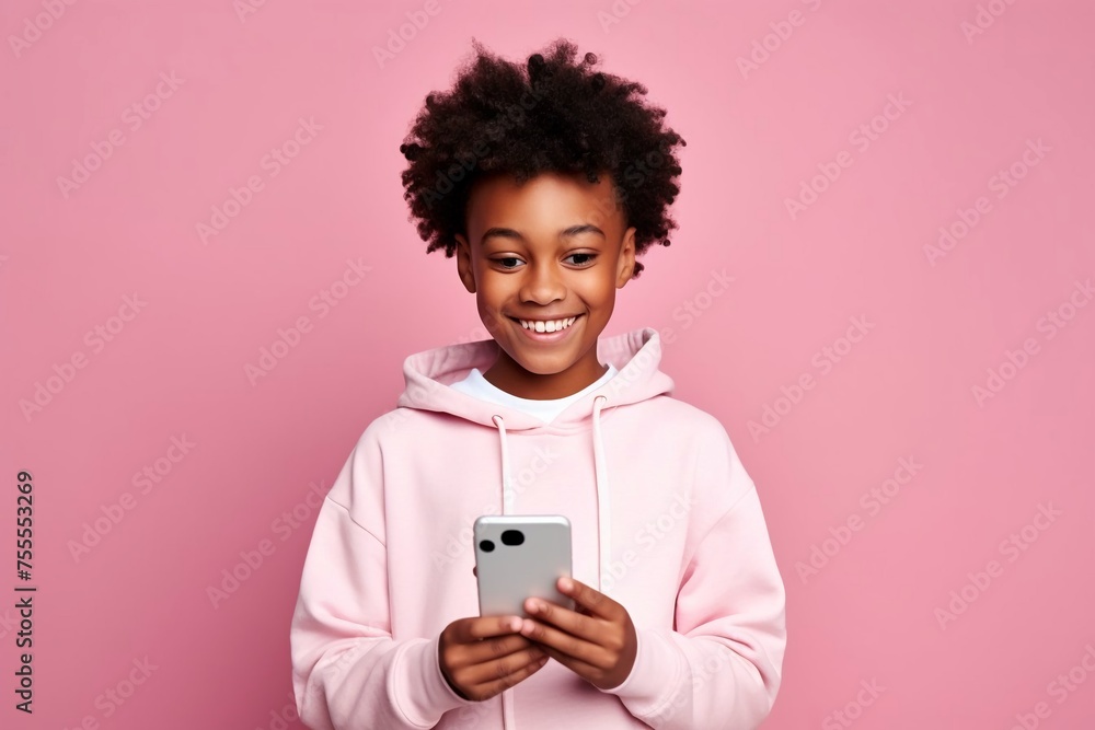 An African-American boy in a light hoodie is looking at his phone, smiling. long afros. on a pink background. An African-American boy in a light hoodie is looking at his phone, smiling. long afros. on a pink background.