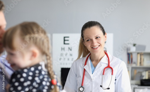 Smiling female doctor standing near little girl in clinic. Medical care for children concept