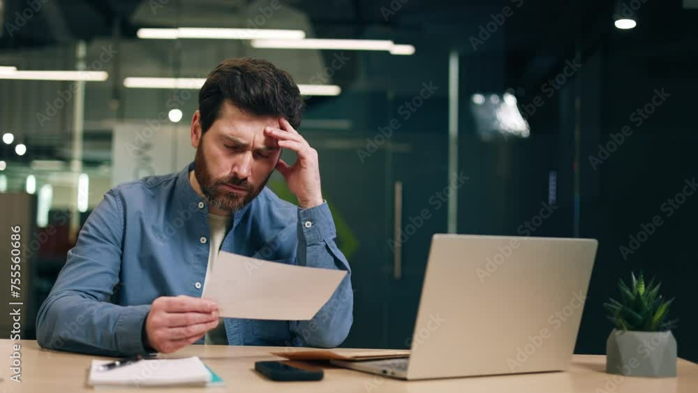 Entrepreneur reading important document and closing eyes while expressing concern about serious problem. Male accountant sitting at desk with laptop and getting formal letter from bank about debt.