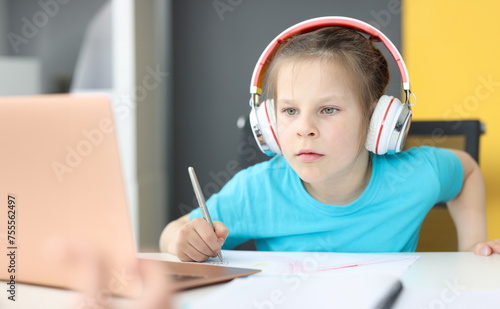 Little girl schoolgirl in headphones sitting in front of laptop at home. Homeschooling concept
