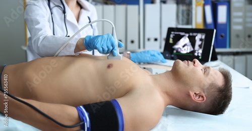 Doctor doing heart ultrasound to young male patient in clinic. Diagnosis and treatment of heart pathology concept