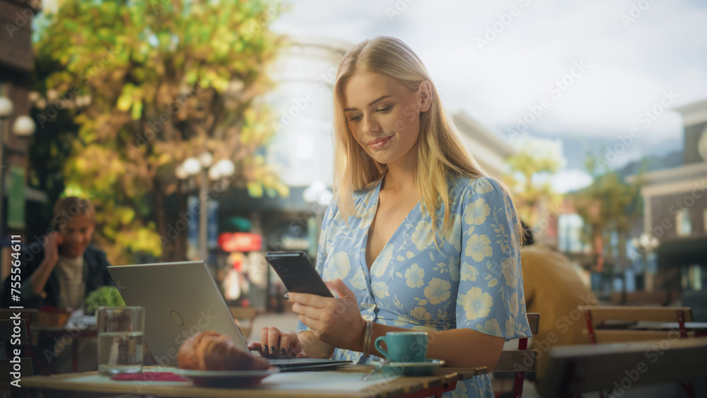 Female Manager Working Remotely on a City Terrace in a Lovely Restaurant. Young Talented Specialist Connected with the Office Team Online, Multitasking Between Laptop and Smartphone Female Manager Working Remotely on a City Terrace in a Lovely Restaurant. Young Talented Specialist Connected with the Office Team Online, Multitasking Between Laptop and Smartphone