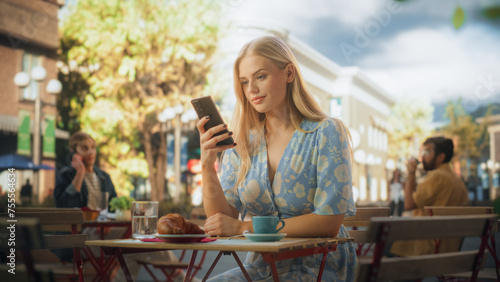 Attractive Female Sitting Alone in a Street Cafe  Having a Cup of Coffee and Croissant. Young Woman Using Smartphone  Chatting with Friends Online  Checking Social Media and Work Emails