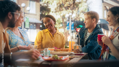 Diverse Group of Friends Enjoying Leisure Time in a Street Cafe. Young Women and Men Sitting Behind a Table, Having Fun and Joyful Conversations. Black African Girl Sharing Motivational Work Stories photo