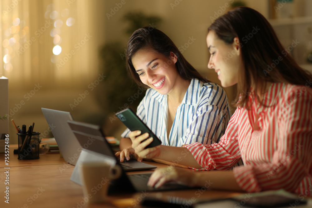 Tele worker showing phone to her colleague in the night Tele worker showing phone to her colleague in the night