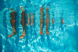 People legs dangling in pool, view from underwater on sunny day