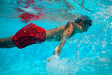 Young boy wear goggles swimming underwater at pool in profile