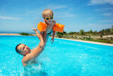 Dad lifting a child high above the water in swimming pool