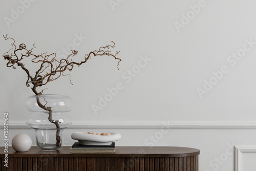 Minimalist composition of living room interior with copy space, wooden sideboard, glass vase with branch, bowl, ball sculpture and personal accessories. Home decor. Template.