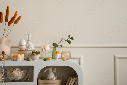 Minimalist composition of easter living room interior with copy space, easter bunny sculpture, easter eggs, vase with dried flowers, wall with stucco and personal accessories. Home decor. Template. © FollowTheFlow
