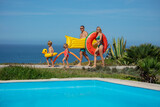 Family head to pool by sea, with floats full height portrait