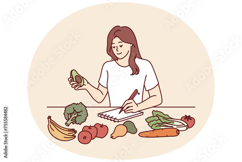 Woman near table with vegetables makes notes in notebook counting calories or making plan for new keto diet. Girl takes care of diet by choosing only organic vegetables grown by farmers