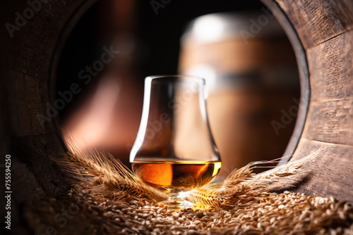 A glass of bourbon whiskey in old oak barrel. Copper alambic and oak barrel on background. Traditional alcohol distillery concept photo