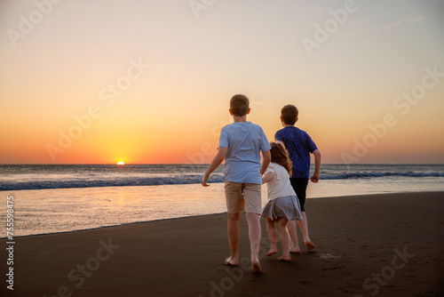 Three kids silhouettes running and jumping on beach at sunset. happy family, two school boys and one little preschool girl. Siblings having fun together. Bonding and family vacation.